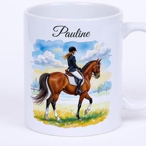 Op de afbeelding: Witte keramische mok met een aquarel illustratie van een ruiter op een bruin paard. De mok heeft de naam "Pauline" in script. De achtergrond toont een blauwe lucht met wolken en een grasveld.