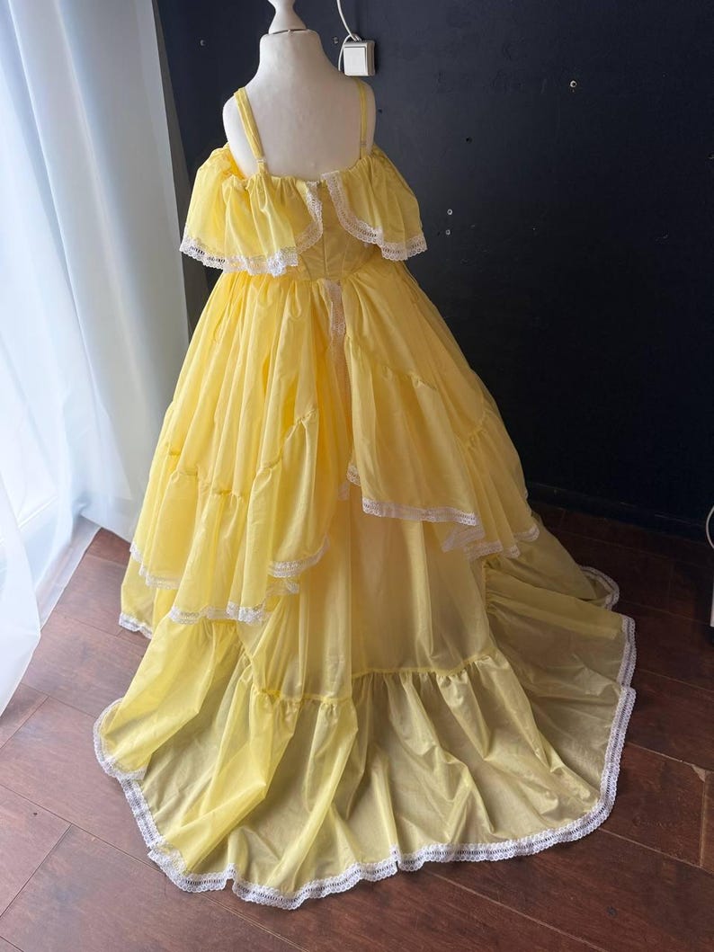 Op de afbeelding: Een felgele, vloerlange jurk met off-shoulder ruche-mouwen, een gelaagde rok en een fijne witte kanten rand langs de mouwen en de zoom. Het lijfje is voorzien van dunne schouderbandjes en heeft een volledig, zwierig silhouet.