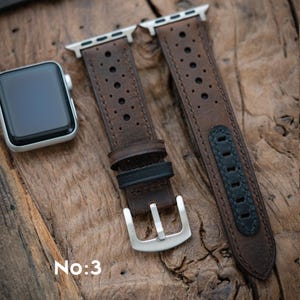 May include: Brown leather watch straps with silver clasps and a black detail. The straps feature a perforated pattern and are shown on a wooden surface. A silver watch is visible on the left. The text "No:3" is at the bottom.