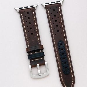 May include: Brown leather watch bands with silver hardware and a black accent. The bands have a perforated design and are displayed on a wooden surface. A silver watch is visible on the left. The text "No:3" is at the bottom.