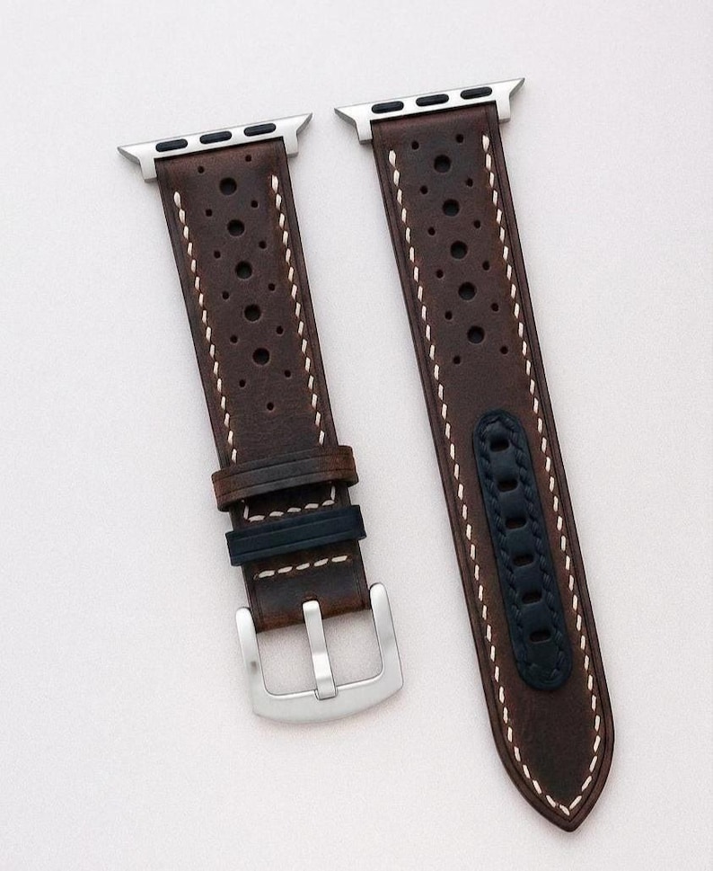 May include: Brown leather watch bands with silver hardware and a black accent. The bands have a perforated design and are displayed on a wooden surface. A silver watch is visible on the left. The text "No:3" is at the bottom.