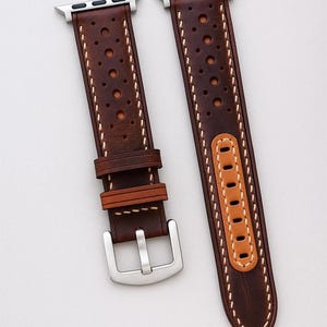 May include: Brown leather watch band with a perforated design and white stitching. The band features a silver buckle and a light brown accent piece. The text "No:1" is visible in the bottom right corner. The watch band is designed for an Apple Watch.
