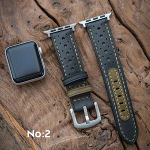 May include: Black leather watch strap with perforated detailing and olive green accents. The strap has a silver buckle and is shown with a silver smartwatch. The text "No:2" is visible.