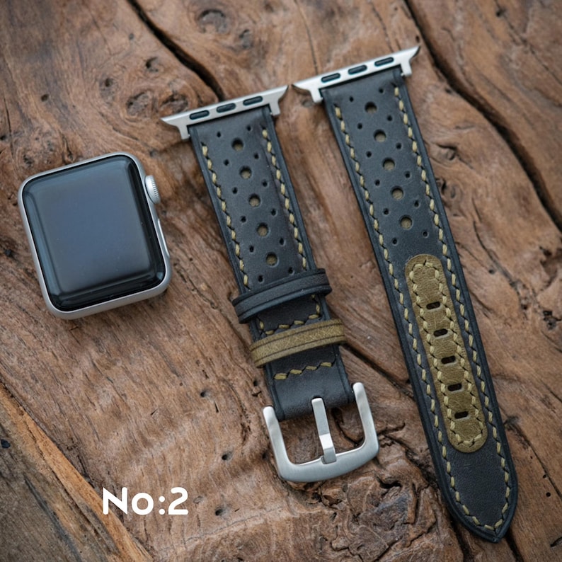 May include: Black leather watch strap with perforated detailing and olive green accents. The strap has a silver buckle and is shown with a silver smartwatch. The text "No:2" is visible.