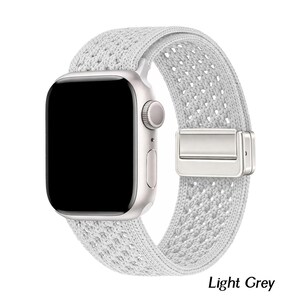 May include: A light grey smartwatch with a rectangular black screen and a silver metallic casing. The watch features a textured, woven fabric band with a matching silver-toned magnetic clasp mechanism. The text Light Grey is visible.