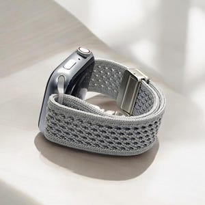 May include: A gray woven Apple Watch band with a silver buckle.
