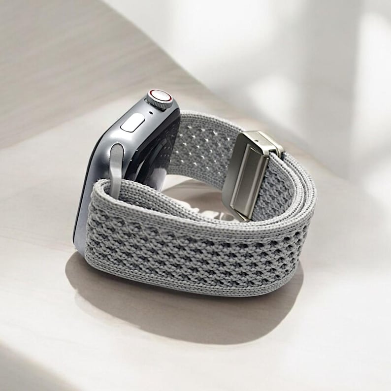 May include: A gray woven Apple Watch band with a silver buckle.