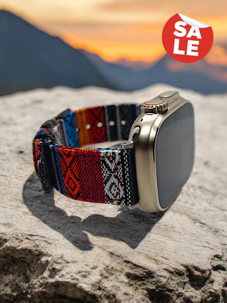May include: A smartwatch with a colorful woven band featuring red, blue, and white patterns. The watch has a metallic case and a black screen. A red circle with the word "SALE" is in the background.