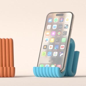 Könnte beinhalten: Ein Smartphone liegt in einem blauen, wellenförmigen Telefonständer. Auf dem Bildschirm des Telefons werden App-Symbole angezeigt. Links befindet sich ein orangefarbenes, geripptes Objekt. Der Hintergrund ist einfarbig hellbeige. Der Telefonständer ist modern gestaltet.