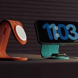 Könnte beinhalten: Zwei Telefonständer, einer orange und einer türkis, mit einem weißen Lade-Pad auf jedem. Der Telefonständer links ist gebogen und der Telefonständer rechts ist gerade. Der Telefonständer rechts hat ein Telefon mit einer digitalen Uhr, die 11:03 anzeigt.