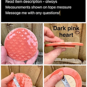 May include: A round dark pink ceramic lid featuring a raised heart pattern. The lid has a smooth, glossy finish. A measuring tape shows the diameter is approximately 3 inches. The underside is unglazed beige ceramic with a circular indentation.