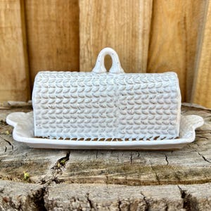 May include: White ceramic butter dish with a textured, woven design. The dish has a lid with a handle and a separate base.