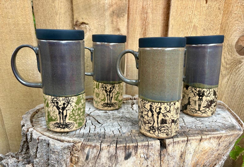 May include: Four tall ceramic mugs with black lids and handles. The upper sections have a smooth, dark grey glaze, while the lower sections feature intricate black line art of skeletal figures intertwined with tree branches on a light background.
