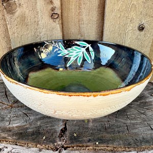 May include: A large, white ceramic bowl with a green and blue glaze. The bowl has a textured exterior and a smooth interior. The bowl is decorated with a green leaf design.