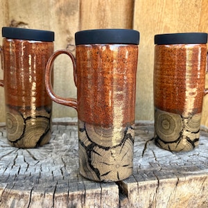 May include: Three tall ceramic mugs with black lids and handles. The upper portion of each mug features a glossy, speckled reddish-brown glaze, while the lower section displays a detailed, dark-toned wood grain pattern resembling cross-cut tree rings.