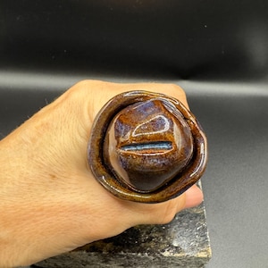 May include: A brown and blue ceramic ring with a textured surface and a small hole in the center.