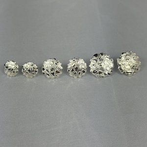 Puede incluir: Seis esferas plateadas de diferentes tamaños con una superficie texturizada y porosa. Las esferas están dispuestas en fila, con un aspecto orgánico y brillo metálico. El fondo es gris claro.