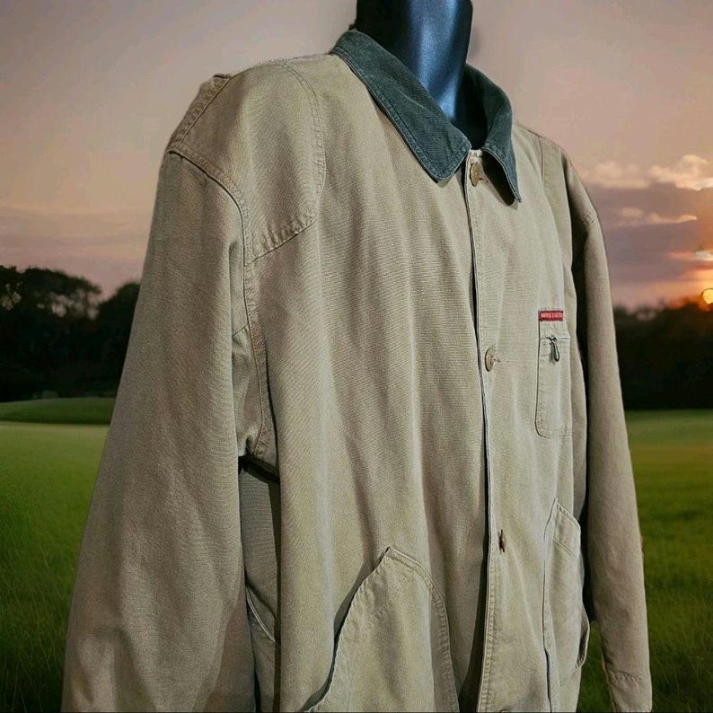 May include: A tan corduroy jacket with a dark green collar. The jacket has two large front pockets and a small red and white logo on the chest. The jacket is buttoned up and displayed on a mannequin.