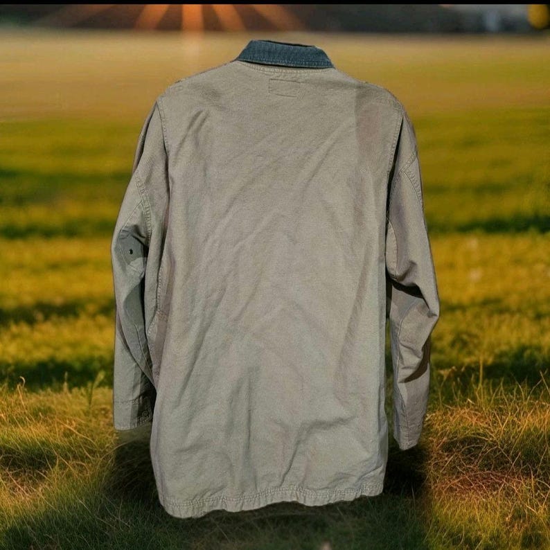 May include: A khaki-coloured jacket with a dark blue denim collar. The back of the jacket is visible, showing the full length and sleeves. The jacket appears to be made of a durable fabric, suitable for outdoor wear.
