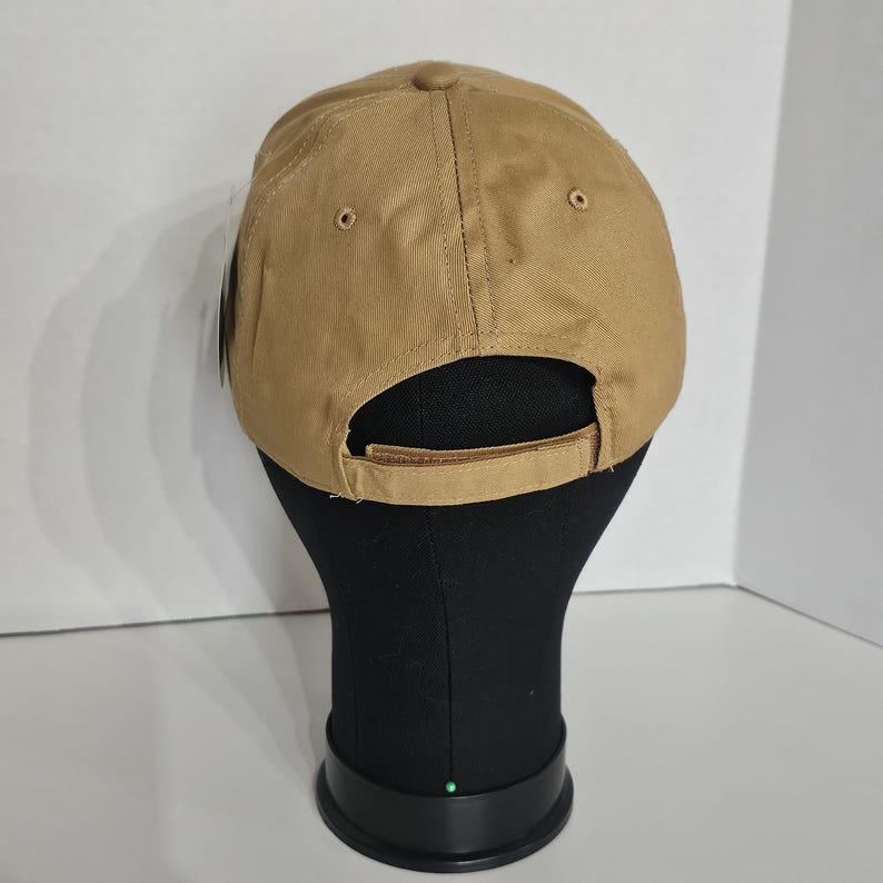 May include: A tan baseball cap with a curved brim. The back of the cap features an adjustable strap and two small ventilation holes. The cap is displayed on a black mannequin head.