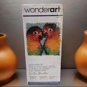 May include: A Wonderart latch hook kit featuring a colorful design of two lovebirds. The kit includes a 12 x 12 inch (30 x 30 cm) pattern. The box has the text "LATCH HOOK KIT" and "Lovebirds".