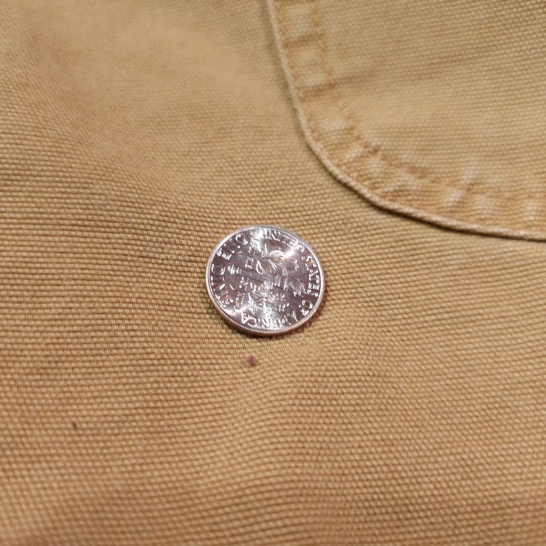 May include: A silver quarter coin featuring an eagle design, placed on a tan fabric. The coin's details are clear, and the fabric has a textured look. The coin is approximately 2.4 cm in diameter.