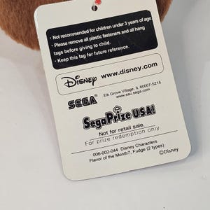 Puede incluir: Una etiqueta blanca con texto de Disney y Sega. La etiqueta incluye advertencias sobre ni&ntilde;os y direcciones de sitios web. Tambi&eacute;n indica "No para la venta al por menor. Solo para canje de premios."