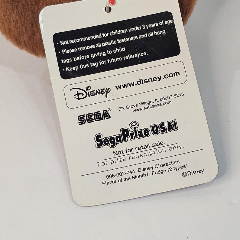Puede incluir: Una etiqueta blanca con texto de Disney y Sega. La etiqueta incluye advertencias sobre ni&ntilde;os y direcciones de sitios web. Tambi&eacute;n indica "No para la venta al por menor. Solo para canje de premios."