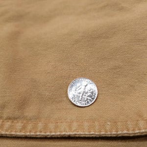 May include: A silver dime coin rests on a tan fabric. The coin is marked with "United States of America" and "One Dime". The fabric has a textured appearance. The image is a close-up.