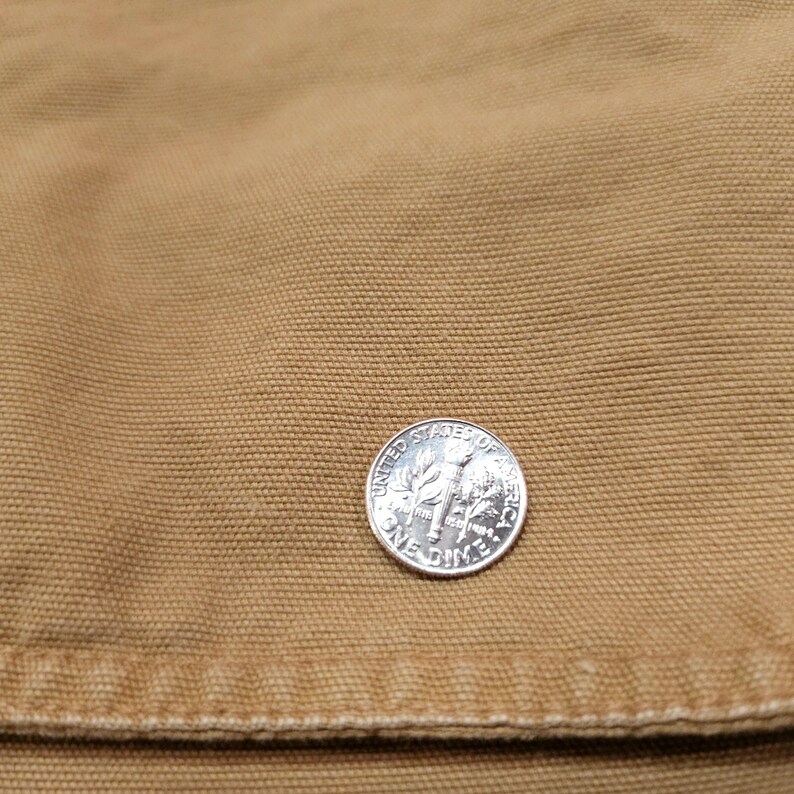 May include: A silver dime coin rests on a tan fabric. The coin is marked with "United States of America" and "One Dime". The fabric has a textured appearance. The image is a close-up.