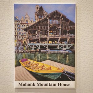 May include: A rectangular magnet featuring a watercolor painting of the Mohonk Mountain House. The image shows a yellow rowboat on a dock in front of the large wooden building. The text "Mohonk Mountain House" is at the bottom.