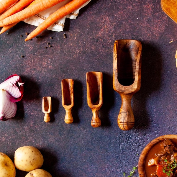 May include: A set of four graduated wooden scoops with a natural grain pattern, arranged in a row from smallest to largest. The scoops feature rounded handles and deep, open bowls, crafted from a light to medium brown wood with visible dark swirls.