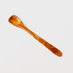 May include: A wooden spoon with a rounded bowl and a long, slender handle. The spoon is made of olive wood, showcasing a warm, natural wood grain pattern. The spoon is designed for cooking and serving.
