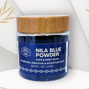 Peut inclure: Un pot de masque pour le visage et le corps Nila Blue Powder avec un couvercle en bois. L'étiquette indique "Nila Blue Powder" et "Nourishes, Smooths & Brightens Skin". Le pot contient 200g de produit.