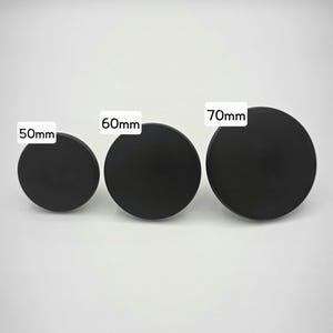 Może przedstawiać: Wyświetlane są trzy czarne, okrągłe obiekty o r&oacute;żnych rozmiarach. Obiekty są oznaczone średnicami: 50 mm, 60 mm i 70 mm. Obiekty znajdują się na gładkim, białym tle.