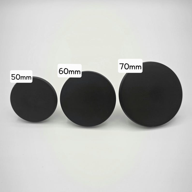 Może przedstawiać: Wyświetlane są trzy czarne, okrągłe obiekty o r&oacute;żnych rozmiarach. Obiekty są oznaczone średnicami: 50 mm, 60 mm i 70 mm. Obiekty znajdują się na gładkim, białym tle.