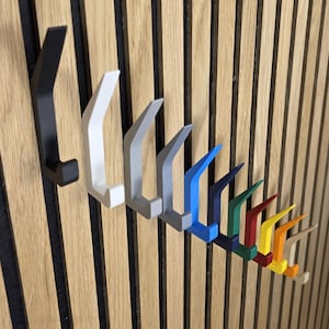 May include: A row of colorful wall hooks in various shades, including black, white, gray, blue, green, red, yellow, orange, and beige. The hooks are mounted on a wooden slatted wall, offering a modern and organized storage solution.