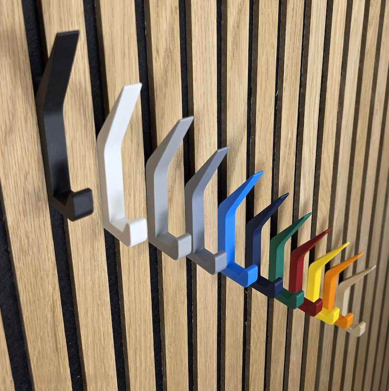 May include: A row of colorful wall hooks in various shades, including black, white, gray, blue, green, red, yellow, orange, and beige. The hooks are mounted on a wooden slatted wall, offering a modern and organized storage solution.