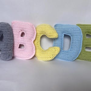 May include: Five crocheted letters, A, B, C, D, and E, in different colors. The letters are gray, pink, yellow, light blue, and green.