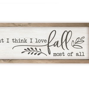 May include: A framed wooden sign with the text "but I think I love fall most of all" in black script font. The sign has a white background and a brown wooden frame.