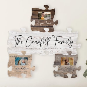 May include: A white wooden sign with the text "The Cranfill Family Established March 7, 2012" and four photo frames shaped like puzzle pieces. The photo frames are filled with pictures of a family.