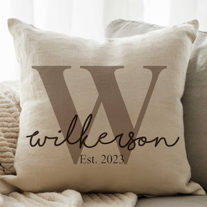 May include: A beige linen pillow with a large brown letter "W" and the text "Wilkerson Est. 2023" in black.