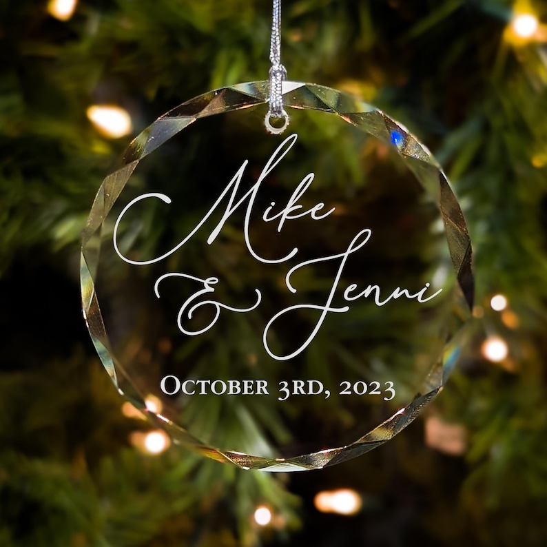 May include: Clear glass Christmas ornament with the names "Mike & Jenni" and the date "October 3rd, 2023" etched in white.