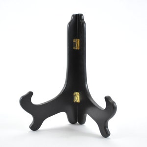 May include: A black wooden easel stand with a simple design. The stand has three legs and a flat top for displaying items.