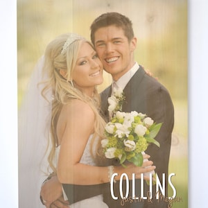 May include: A wedding photo of a couple, the bride is wearing a white dress and a tiara, the groom is wearing a black suit, the couple is holding a bouquet of white flowers, the photo is printed on a wooden background with the text "COLLINS Justin & Megan"