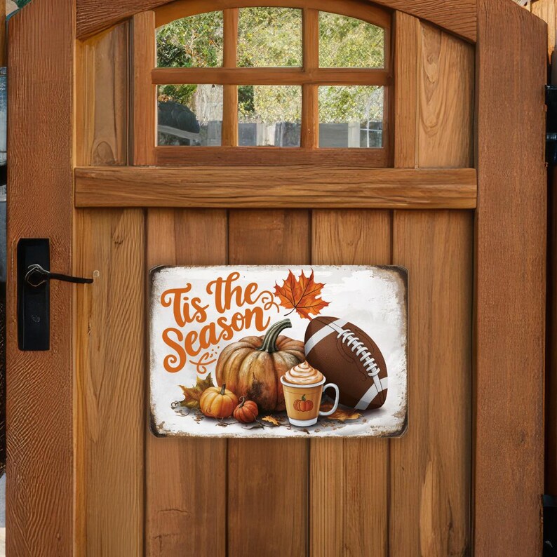 May include: A white sign with the text "Tis the Season" and a fall-themed illustration of pumpkins, a football, and a cup of coffee.