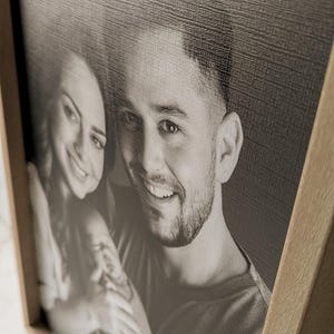 May include: A black and white photograph of a couple in a wooden frame. The man is smiling and the woman is looking at the camera.