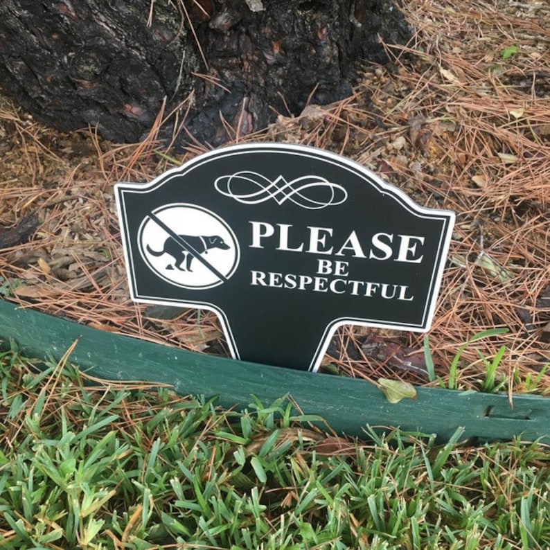 A small yard sign with the message Please Be Respectful and a no dog pooping symbol.  It has a stake that is used to plant the sign in the ground.  A sleek black finish with bright white text makes this sign a very attractive addition to your yard.