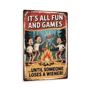 May include: A rectangular metal sign with a distressed finish. The sign features a cartoon illustration of three boys roasting hot dogs over a campfire. Text at the top reads "IT'S ALL FUN AND GAMES" and at the bottom "...UNTIL SOMEONE LOSES A WIENER!"