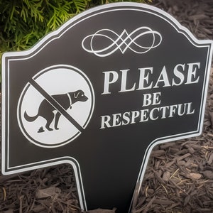A small yard sign with the message Please Be Respectful and a no dog pooping symbol.  It has a stake that is used to plant the sign in the ground.  A sleek black finish with bright white text makes this sign a very attractive addition to your yard.